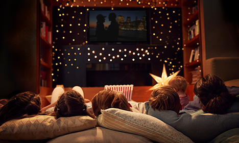 a family laying on pillows and watching a TV screen. One person is holding popcorn