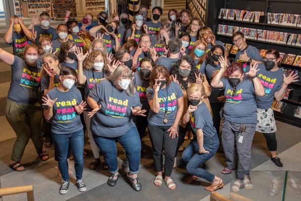 A few dozen library staff members, all wearing the summer reading t-shirt that says "Read, Read, Read" posed for a silly group photo. 